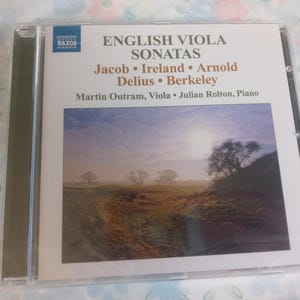 May include: A CD case for "English Viola Sonatas" by Jacob, Ireland, Arnold, Delius, and Berkeley. The cover shows a landscape with trees and a cloudy sky. The CD is in a clear plastic case.