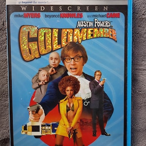 May include: DVD of the movie "Austin Powers in Goldmember". The cover features Mike Myers, Beyoncé Knowles, and Michael Caine. The title is in a gold, glittery font. The background is blue with several characters from the film.