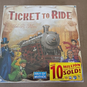 May include: A square board game box titled Ticket to Ride by Alan R. Moon. The cover features a large steam locomotive, several people in vintage attire, and a yellow sticker stating Over 10 Million Ticket to Ride Games Sold in red text.