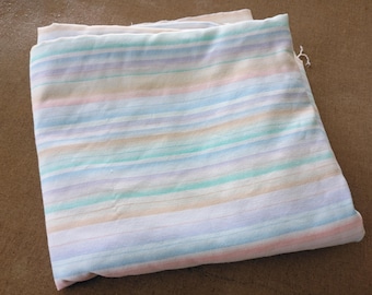 Op de afbeelding: Een gevouwen stuk stof met een horizontaal gestreept patroon in zachte pasteltinten van lichtblauw, perzik, lavendel en mintgroen tegen een witte achtergrond. Het textiel heeft een gladde textuur en is netjes op een stapel gelegd.
