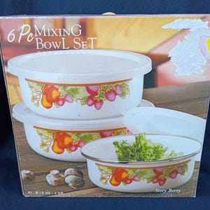 May include: A 6-piece mixing bowl set with white bowls and lids. The bowls have a decorative border with illustrations of fruit and leaves. One bowl contains lettuce. The box reads "6 Pc Mixing Bowl Set".