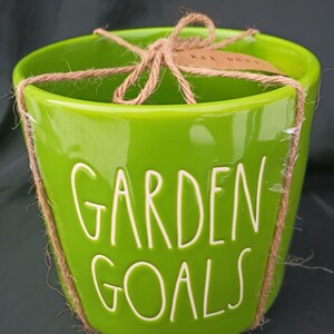 Peut inclure: Un pot de fleurs en céramique vert vif avec l'inscription blanche "GARDEN GOALS". Il est noué avec de la ficelle et comporte une petite étiquette. Le pot est conçu pour le jardinage.