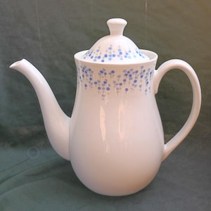 Op de afbeelding: Witte keramische theepot met een afgeronde body, gebogen tuit en een handvat. Het deksel en het bovenste deel van de theepot zijn versierd met een blauw bloemmotief. De theepot is ontworpen voor het serveren van thee.