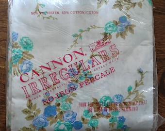 Puede incluir: Una sábana plana doble empaquetada con un estampado floral de rosas azules y turquesas sobre un fondo blanco. El embalaje dice "Cannon Irregulars" y "No-Iron Percale". La sábana está diseñada para un colchón de 99 cm.