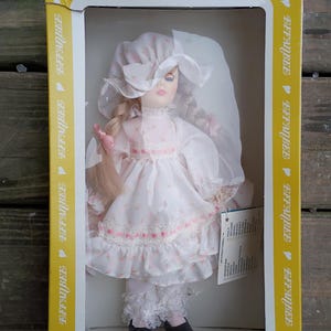 May include: A vintage Effanbee doll in its original box. The doll is dressed in a white dress with pink floral accents, a matching bonnet, and black shoes. The box is yellow with the Effanbee logo.