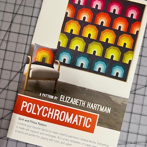 May include: A quilt pattern book titled "Polychromatic" by Elizabeth Hartman. The cover features a colorful rainbow quilt block with a pillow in the same pattern.
