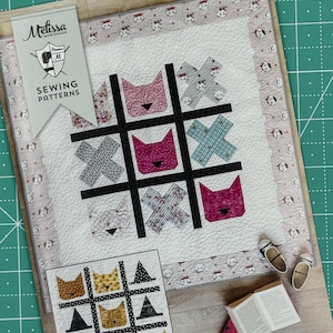 May include: A sewing pattern for a quilt featuring a noughts and crosses board with cat faces. The pattern includes a smaller version of the quilt with a black and white background and yellow cat faces. The text "Tic Tac Cat" is printed on the bottom of the pattern.