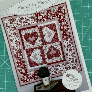 Puede incluir: Patrón de acolchado para una colcha roja y blanca con un diseño de corazón a corazón. La colcha mide 91,44 cm por 91,44 cm. El patrón se llama "Heart to Heart" y está diseñado por Jill Finley. El número de patrón es 1951.