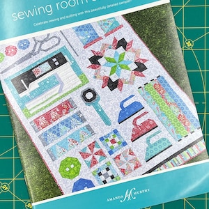 May include: A blue and white booklet with the title "Sewing Room Sampler 2" and the text "Celebrate sewing and quilting with this beautifully detailed sampler!"  The booklet features a colorful quilt design with various sewing and quilting tools.