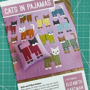 May include: A quilting pattern for a quilt and pillow featuring cats wearing pajamas. The pattern is called "Cats in Pajamas" and is by Elizabeth Hartman. The pattern uses fat quarters and traditional patchwork techniques.