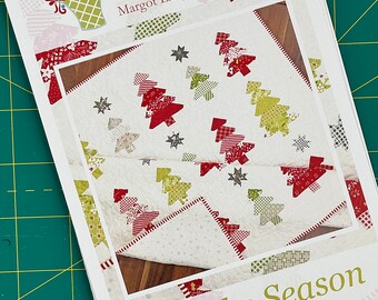 Może przedstawiać: Biała kołdra z tkaniny z patchworkowym wzorem czerwonych i zielonych choinek i gwiazd. Kołdra nosi tytuł "Tis the Season" i pochodzi z The Pattern Basket, Margot Languedoc Designs.