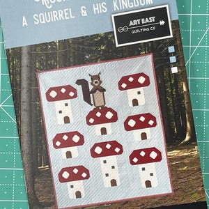 May include: A quilt pattern titled "Mushroom King, A Squirrel & His Kingdom." The design features a squirrel atop a mushroom, surrounded by other mushroom houses. The quilt measures 40" x 48". The cover includes the Art East Quilting Co. logo.