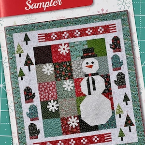 May include: A winter-themed quilt sampler featuring a snowman in the center surrounded by trees, mittens, and snowflakes. The quilt is made with a variety of fabrics in red, green, white, and black. The quilt is titled "Winter Wonder Sampler" and is by "Anka's Treasures".