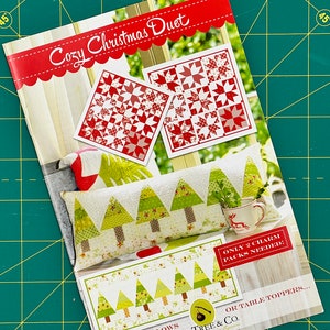 May include: A sewing pattern booklet for a Cozy Christmas Duet featuring a red and white star quilt block design and a green and white tree quilt block design. The pattern is for a set of pillows or table toppers. The text on the cover reads "Cozy Christmas Duet" and "Only 2 Charm Packs Needed: A Duet of Pillows or Table Toppers... Fig Tree & Co."