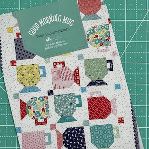 May include: A Good Morning Mug table runner pattern by Lori Holt of Bee in My Bonnet. The pattern features a white background with a repeating design of colorful mugs.