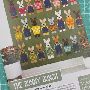 May include: A patchwork quilt pattern featuring a collection of bunnies dressed in various outfits, including shirts, overalls, and dresses. The pattern is titled "The Bunny Bunch: Patchwork Sampler Quilts in Two Sizes".