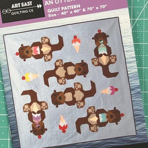 May include: A quilt pattern titled "Cool Treats: An Otter Quilt" featuring brown otters and ice cream cones on a light blue background. The pattern size is 40" x 40" and 70" x 70". The Art East Quilting Co. logo is visible.