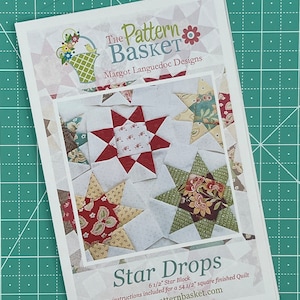 May include: A white paper pattern titled "Star Drops" by The Pattern Basket, featuring star quilt block designs. The pattern includes instructions for a 16.5 cm star block and a 138.4 cm square finished quilt. The website www.thepatternbasket.com is also visible.
