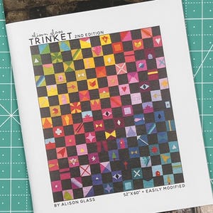 May include: A colorful quilt pattern called "Trinket" by Alison Glass. The pattern is a checkerboard design with a variety of small geometric shapes in bright colors. The pattern is 52 inches by 60 inches and can be easily modified.