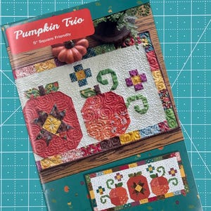 May include: A quilting pattern booklet titled "Pumpkin Trio" featuring a colorful patchwork design with three pumpkins. The pattern is 5-inch square friendly and by Anka's Treasures.