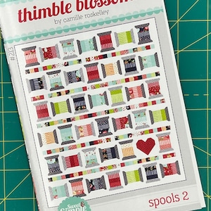 Puede incluir: Un patrón de acolchado para una colcha llamada "Spool 2" de la colección "Thimble Blossoms" de Camille Roskelley. El patrón es una colcha de tiras con un corazón en el centro. El patrón está etiquetado como "Sweet & Simple" y es compatible con rollos de tela.