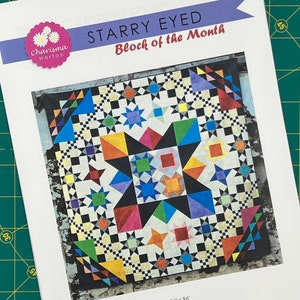 以下が含まれることがあります： Charisma Hortonによる「Starry Eyed Block of the Month」というタイトルのキルトの印刷パターン。キルトのデザインは、さまざまな幾何学的な形をしたカラフルな星のパターンを特徴としています。完成したキルトのサイズは244 x 244 cmです。