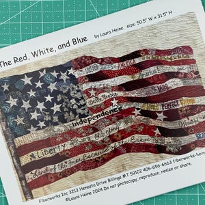 May include: A quilt pattern featuring a red, white, and blue American flag with the words "We the People", "Independence", "Liberty", "Land of the Free Because of the Brave", and "Old Glory" written on it. The quilt is 50.5 inches wide and 31.5 inches high.