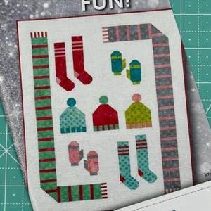 May include: A quilt pattern featuring winter-themed designs, including scarves, mittens, hats, and socks. The pattern is called "Frosty Fun!" and is by Atkinson Designs.