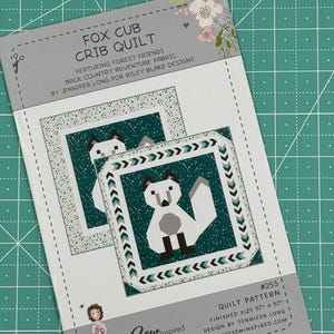 Puede incluir: Un patrón de edredón de cuna de zorro blanco y verde con una ilustración de zorro y el texto "Fox Cub Crib Quilt" y "#253 Quilt Pattern".