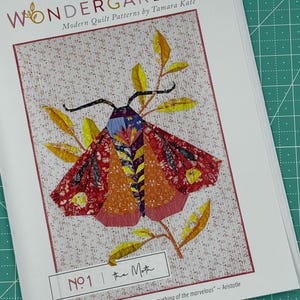 May include: A quilt pattern featuring a colorful moth with yellow, orange, red, and purple wings. The moth is perched on a branch with green leaves. The pattern is titled "The Moth" and is part of the "Wondergarden" collection of modern quilt patterns by Tamara Kate.