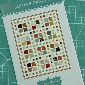 May include: A quilt pattern titled "Square Dance #709" by Gigi's Thimble Quilt Patterns. The pattern features a colourful patchwork quilt with a variety of fabrics and designs.