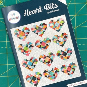 May include: A quilt pattern booklet titled "Heart Bits" by Sew Mariana. The cover features a colourful patchwork design of hearts made from triangles. The booklet is precut and scrap friendly and includes baby and throw sizes.