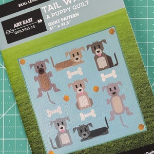 May include: A quilt pattern featuring a design of nine playful puppies with wagging tails. The pattern is titled "Tail Wags" and is a puppy quilt. The pattern is 51 inches by 51.5 inches.