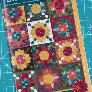 May include: A colorful quilt pattern called "Zinnia Seeds" by Anka's Treasures. The pattern is fat quarter friendly and includes multiple sizes. The pattern features a variety of floral designs in shades of red, yellow, green, and brown.