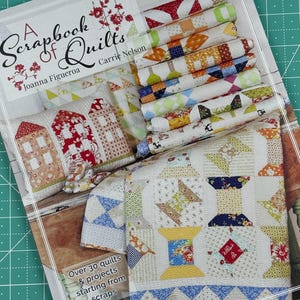 May include: A book titled "A Scrapbook of Quilts" by Carrie Nelson and Joanna Figueroa. The cover features a variety of colorful quilts and quilt blocks. The book includes over 30 quilt projects starting from scraps.