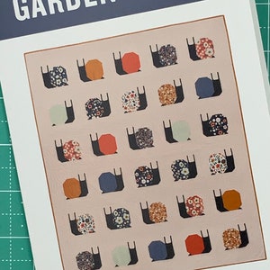 May include: A quilt pattern titled "Garden Snails" featuring a traditional pieced design with a variety of floral and geometric patterns. The pattern is for an intermediate sewist and up.