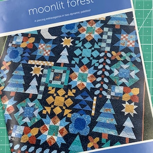 May include: A quilting pattern book cover featuring a colorful quilt with a dark blue background. The quilt features a variety of geometric shapes, including stars, trees, and flowers. The title of the pattern is "Moonlit Forest" and the book is by Amanda Murphy.