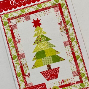 May include: A quilting pattern for a Christmas tree quilt. The pattern features a green and red patchwork tree with a red star on top. The pattern is called "Oh Christmas Tree" and is by Fig Tree & Co. by Joanna Figueroa.