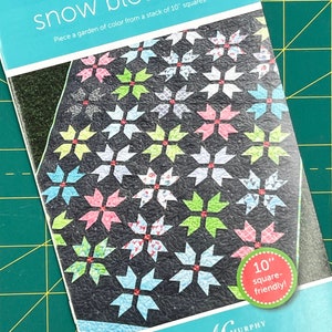 May include: A quilting pattern booklet titled "Snow Blossoms" featuring a colourful quilt design with a black background. The quilt is made from 10-inch squares and is described as "square-friendly".
