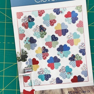 May include: A quilting pattern booklet featuring a colourful quilt design with a clover pattern. The title of the pattern is "Clover" and the booklet is from Cluck Cluck Sew. The quilt is a layer cake or fat eighth quilt in 4 sizes.