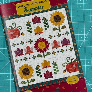 May include: A colorful quilt pattern booklet titled "Autumn Afternoon Sampler" by Heather Patterson for Anka's Treasures. The booklet features a precut friendly design with a variety of autumnal motifs, including pumpkins, sunflowers, and leaves.