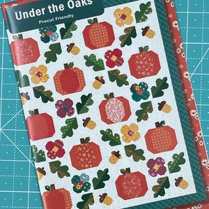 May include: A precut-friendly quilt pattern titled "Under the Oaks" featuring a repeating pattern of red pumpkins, green leaves, yellow and purple flowers, and acorns. The cover has a red floral border and the designer's name, Heather Peterson, is visible.