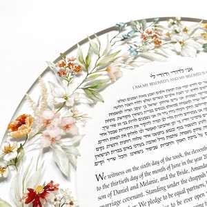 May include: A watercolor illustration of a floral wreath surrounding a ketubah, a Jewish marriage contract. The text in Hebrew reads "I am my beloved's and my beloved is mine." The ketubah is decorated with delicate floral details in shades of pink, white, and orange.
