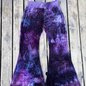 May include: High-waisted velvet bell-bottom pants featuring a tie-dye pattern in shades of deep purple, black, and dark blue. The fabric has a soft, crushed texture throughout, with a wide waistband and flared legs that widen toward the hem.