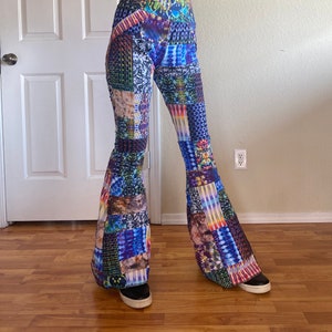 Op de afbeelding: High-waisted broek met uitlopende pijpen en een levendig, veelkleurig patchworkontwerp. De stof toont een verscheidenheid aan ingewikkelde patronen, waaronder tie-dye, geometrische vormen en abstracte texturen in blauwe, paarse, gele en groene tinten.