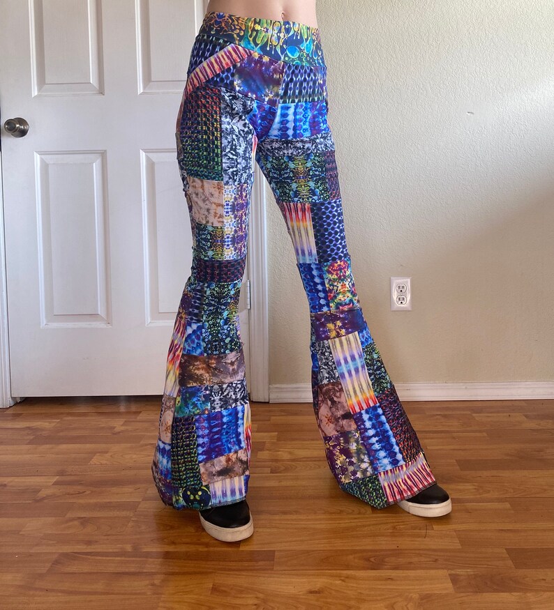 Op de afbeelding: High-waisted broek met uitlopende pijpen en een levendig, veelkleurig patchworkontwerp. De stof toont een verscheidenheid aan ingewikkelde patronen, waaronder tie-dye, geometrische vormen en abstracte texturen in blauwe, paarse, gele en groene tinten.