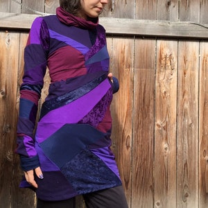 Peut inclure: Une robe à manches longues avec un motif patchwork dans des tons de violet, bleu et bordeaux. La robe a un col montant et une silhouette ajustée.