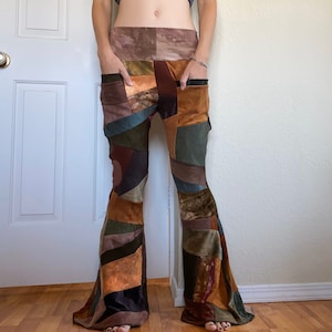 Peut inclure: Pantalon évasé en patchwork doté d'une large ceinture et de poches avant profondes. Le vêtement est composé de divers panneaux de tissu dans des tons marron, vert olive, beige et bordeaux foncé, créant un aspect géométrique texturé.