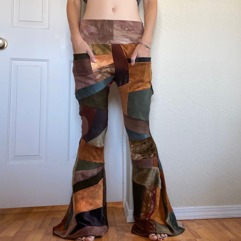 Op de afbeelding: Patchwork broek met wijde pijpen, een brede tailleband en diepe voorzakken. Het kledingstuk is opgebouwd uit diverse stoffen panelen in tinten bruin, olijfgroen, beige en donkerbordeaux, wat zorgt voor een geometrische, textuurrijke uitstraling.