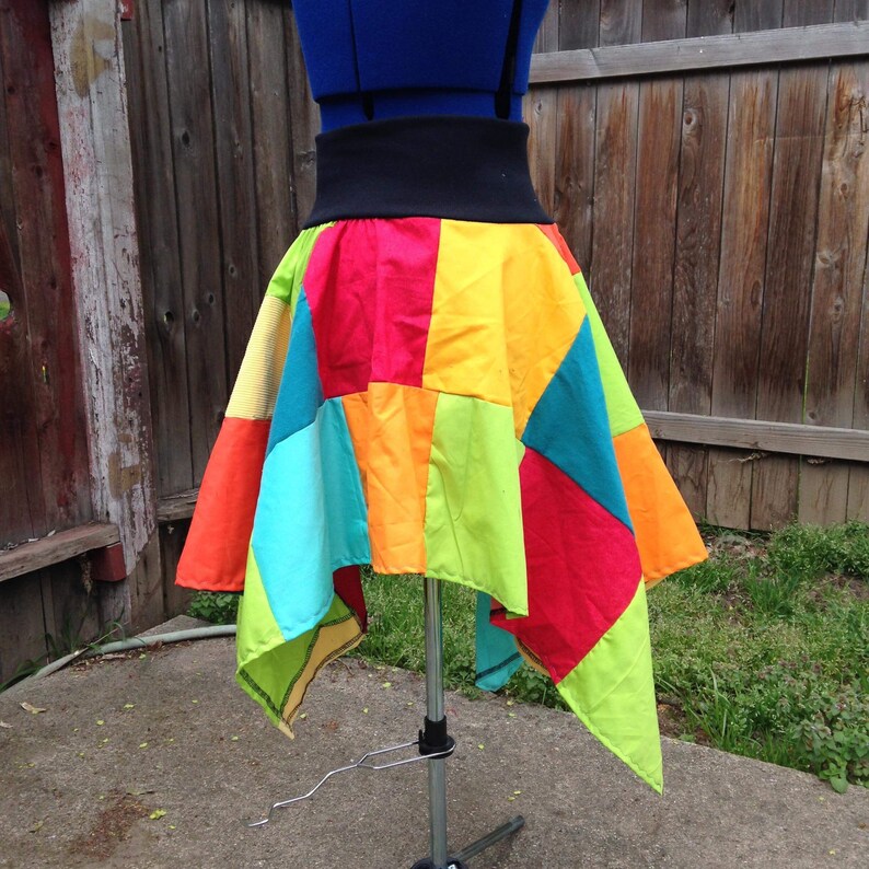 K&ouml;nnte beinhalten: Ein bunter Patchwork-Rock mit einem schwarzen Bund. Der Rock besteht aus verschiedenen Stoffen in verschiedenen Farben, darunter Rot, Orange, Gelb, Gr&uuml;n, Blau und T&uuml;rkis. Der Rock ist asymmetrisch, eine Seite ist l&auml;nger als die andere.